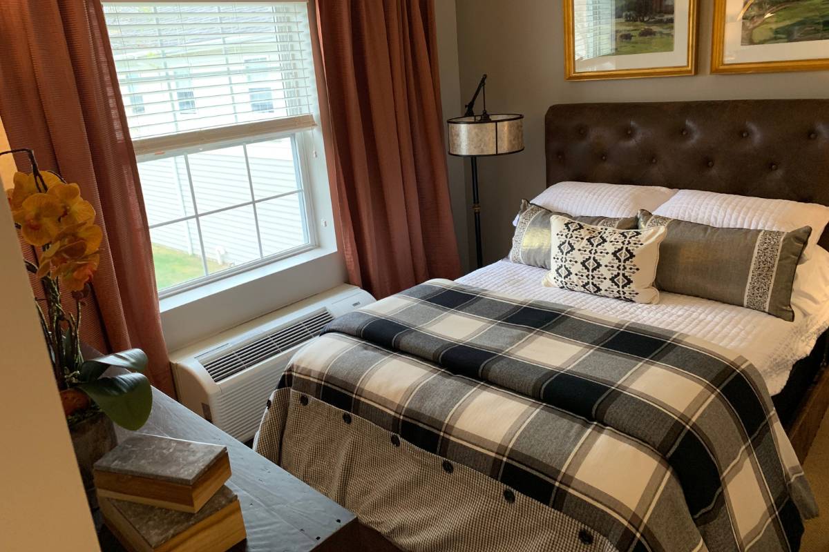 A model bedroom at Dresher Estates, decorated, with a dresser, lamp, and painting, with a bed in the center of the room
